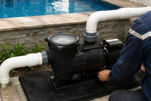 A professional outdoor pool equipment installation showing a HYBSUN solar pump system operating correctly beside a clear swimming pool. The black pool pump is installed on a stable platform with clean white PVC pipes securely connected to the inlet and outlet ports, allowing smooth water circulation through the pool system. The transparent pump basket is filled with water without visible air bubbles, while strong water flow is maintained through the connected return lines. A technician is inspecting the running pump to ensure reliable performance and proper operation. This realistic pool pump system installation demonstrates how a solar powered pond pump or solar water pump should look when working efficiently in an outdoor environment. The HYBSUN solar pump design provides stable water circulation, energy efficient operation, and dependable performance for residential and commercial water applications.